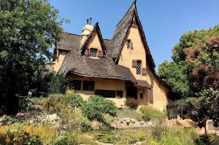 A yellow house with a brown roof and a stone wall.