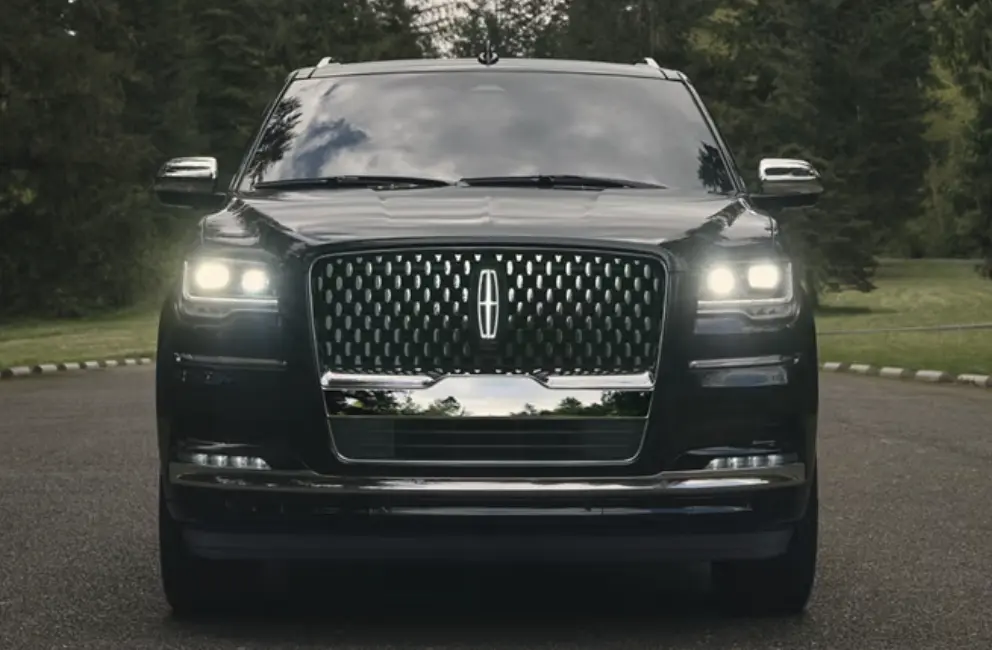 A black suv driving down the street with its headlights on.