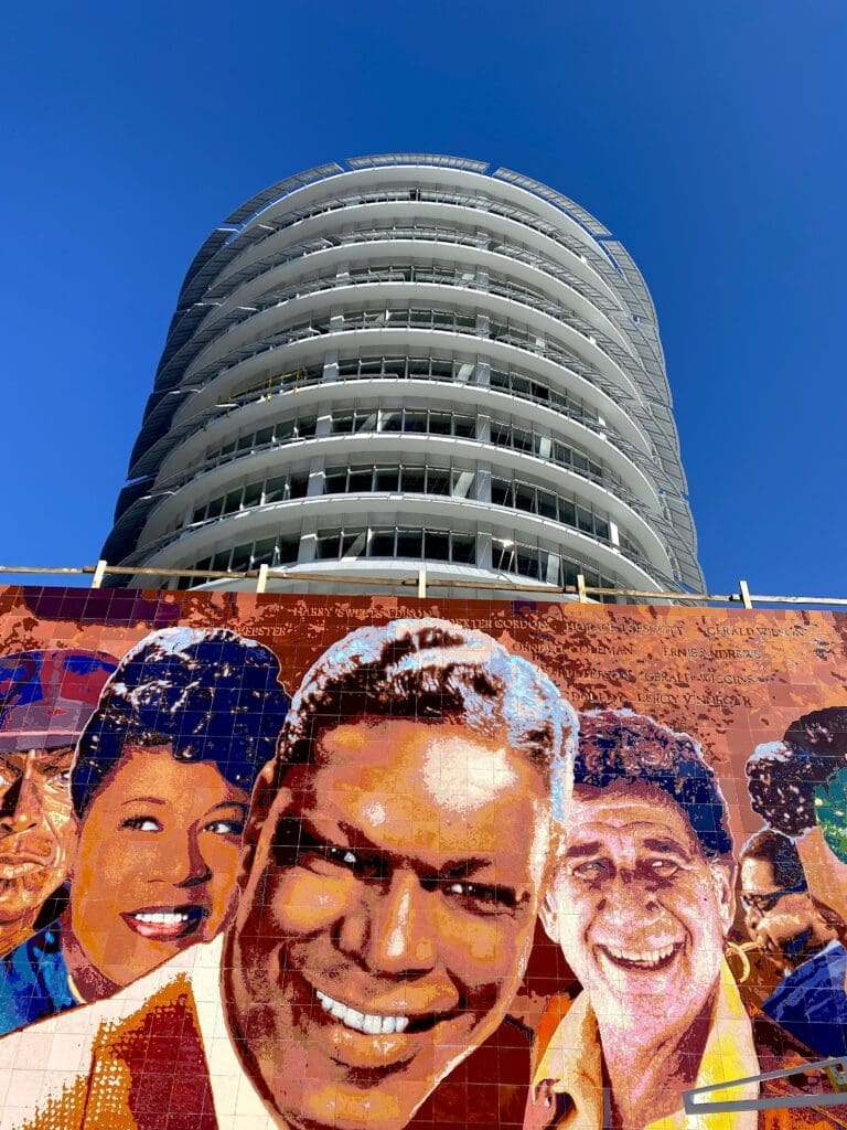 Cylindrical modern building above colorful mural of faces