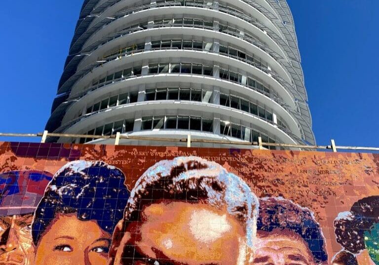Cylindrical modern building above colorful mural of faces
